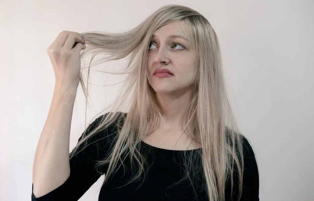 Woman in a black shirt frowning at her hair while holding locks of it while thinking it is a bad hair day.