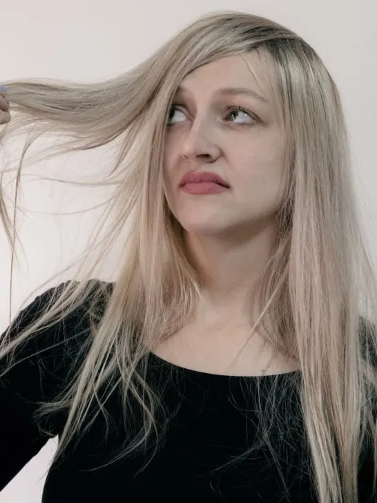 woman in a black shirt frowning at her hair while holding locks of it while thinking it is a bad hair day.
