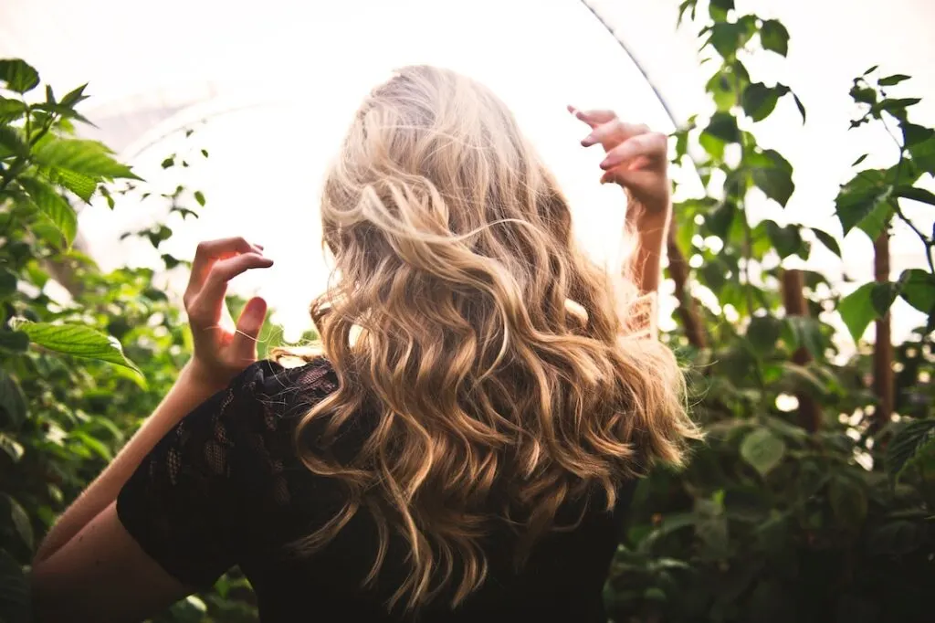 The back side of a woman with beautiful blonde, wavy hair walking through nature. 