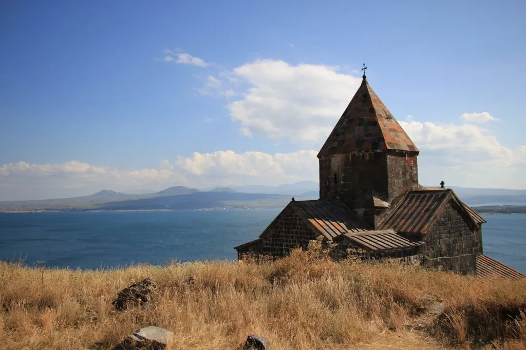 A photo of Lake Sevan taken from above on one of the surrounding mountains with an ancient building in the foreground. Lake Sevan is a popular destination when exploring Armenia.