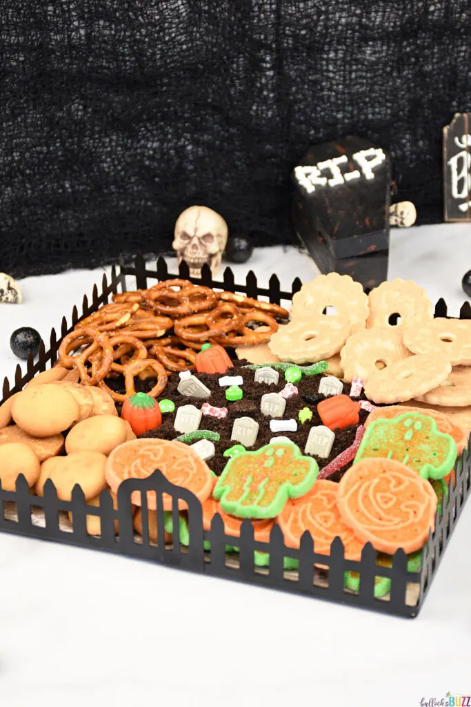 A Halloween Frosting Board graveyard where cookie dirt-covered frosting is decorated with candy tombstones, skulls, pumpkins and gummy worms and surrounded by an eerie selection of sweets for dipping. 