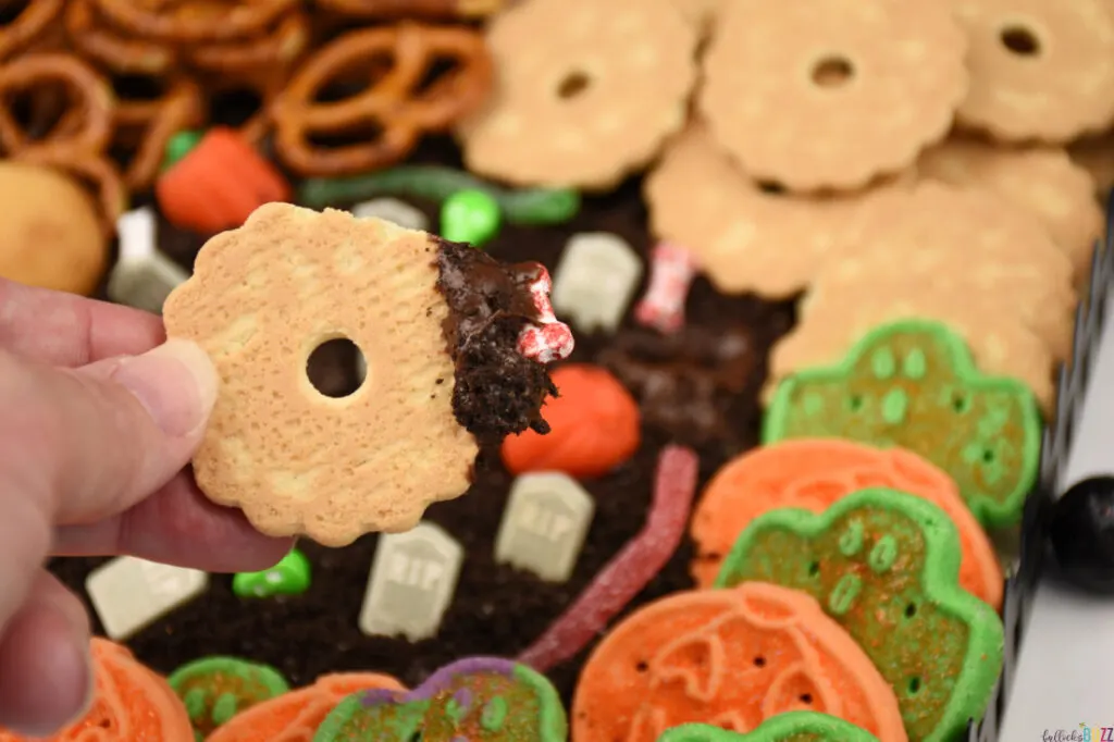 Fingers holding a cookie that has been dipped in the chocolate frosting on the Halloween Frosting Board.