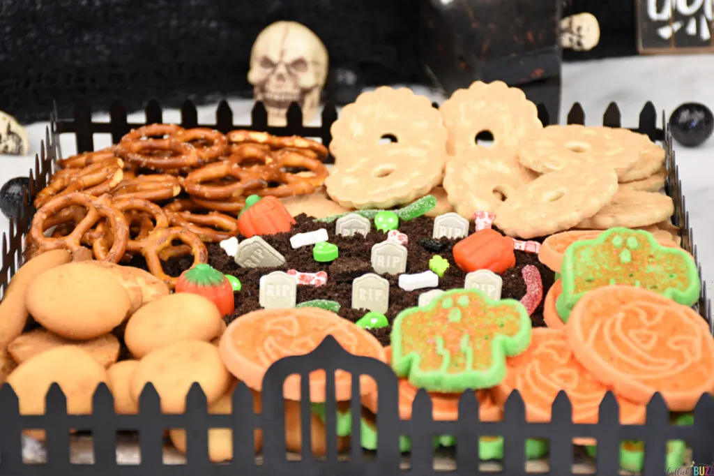 Cookies and pretzels surrounding a graveyard made of frosting and candy on a Halloween Frosting Board.