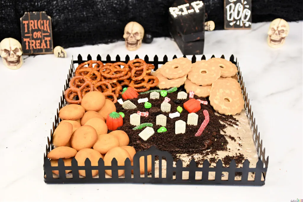 Cookies and pretzels being added to graveyard Halloween frosting board.