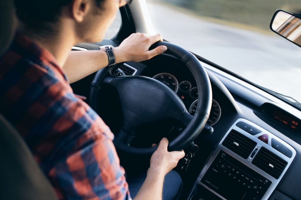 A teenage boy driving. Parents need to use these tips when helping your teen plan their first road trip.