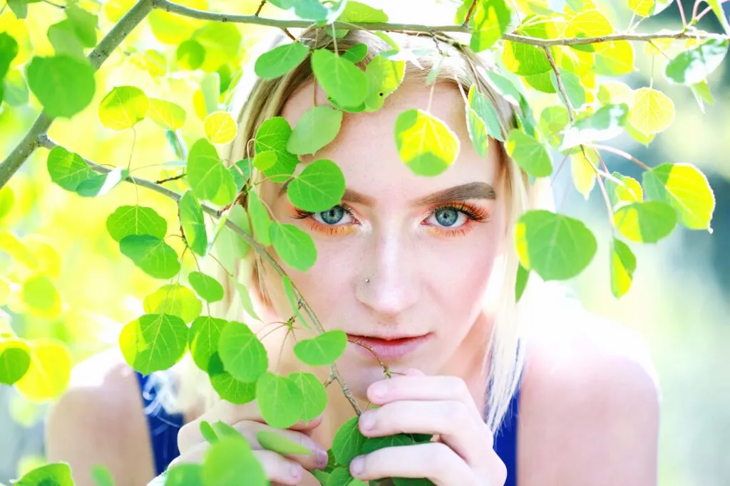 woman with pretty eyes looking around some leaves.