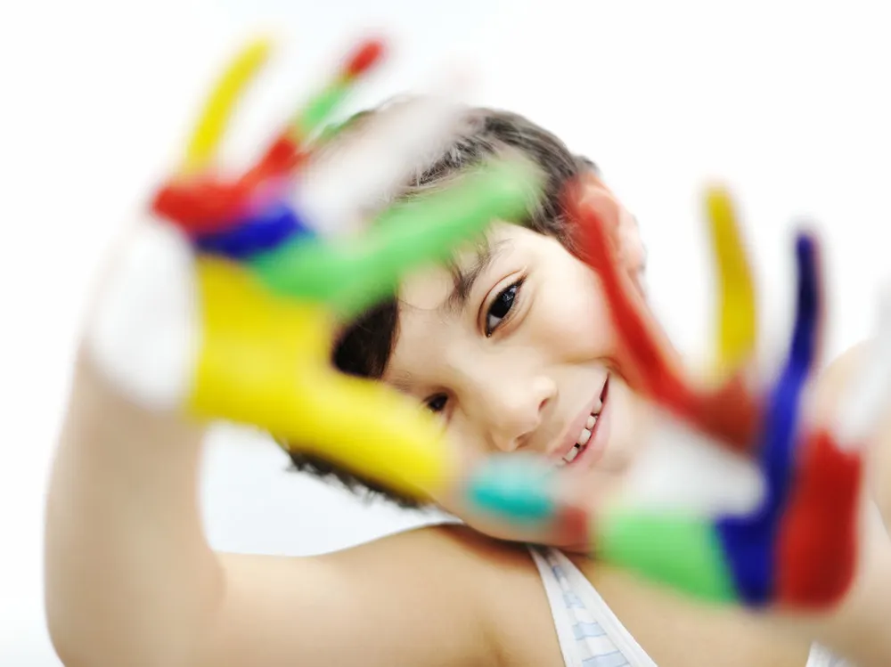 Little boy with hands painted in colorful paints ready to make hand print crafts as a way to encourage creativity in children