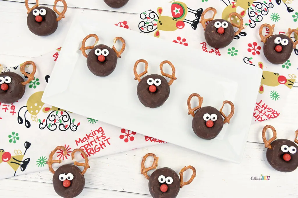 Several finished Reindeer Donuts with pretzel antlers, candy eyes, and a red candy nose on a Christmas background