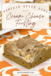 A slice of Pumpkin Spice Bars with Creamy Cheese Frosting on a piece of wax paper sitting on an orange and white tablecloth