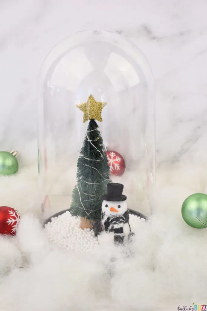 A festive Christmas Cloche, surrounded by faux snow and ornaments, bringing holiday cheer to your decor.