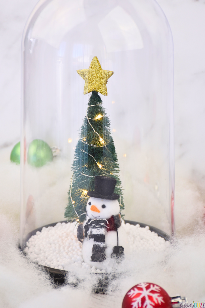A festive Christmas Cloche surrounded by faux snow and ornaments
