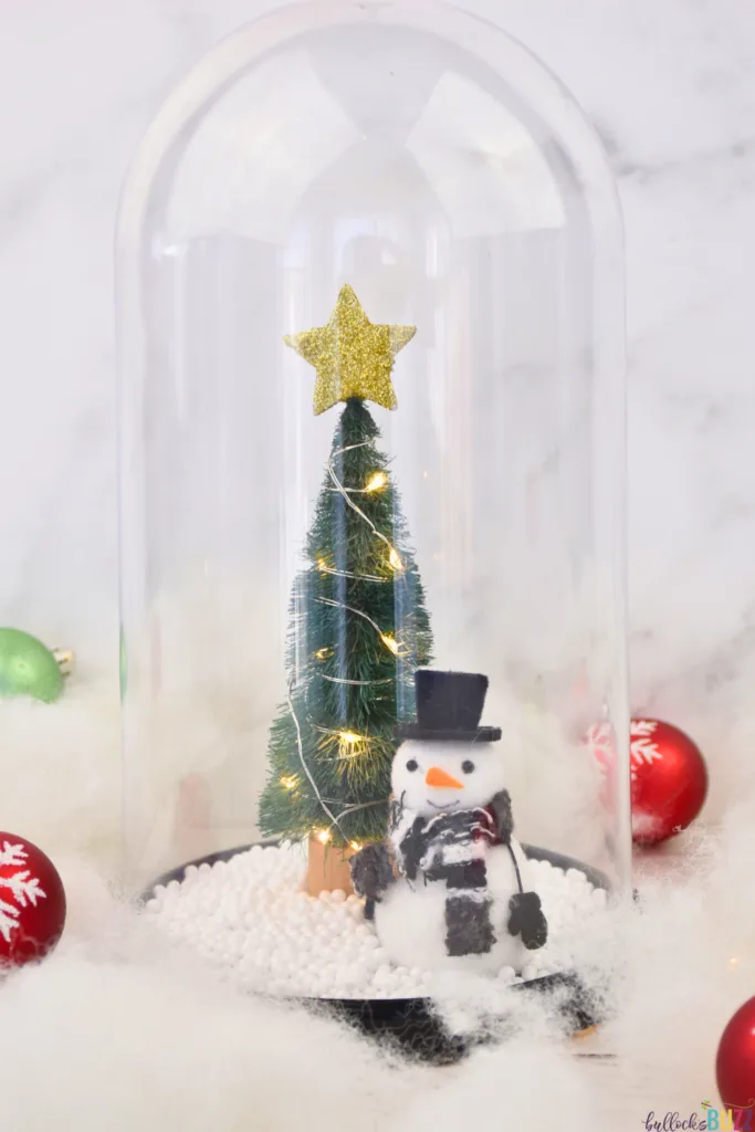 A mini Chriustmas tree and snowman are part of a winter scene created in this DIY Christmas Cloche