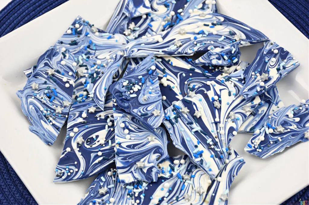 Close-up view of exquisite Hanukkah Candy Bark on a pristine white plate, showcasing vibrant blue and white swirls with festive candy sprinkles—a delightful holiday treat