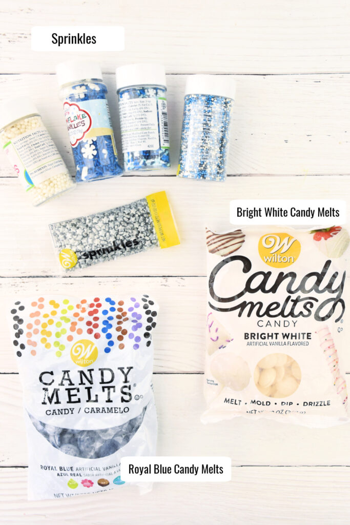 Ingredients needed to make Hanukkah candy bark including an assortment of sprinkles, royal blue candy melts, and bright white candy melts placed on a white background.