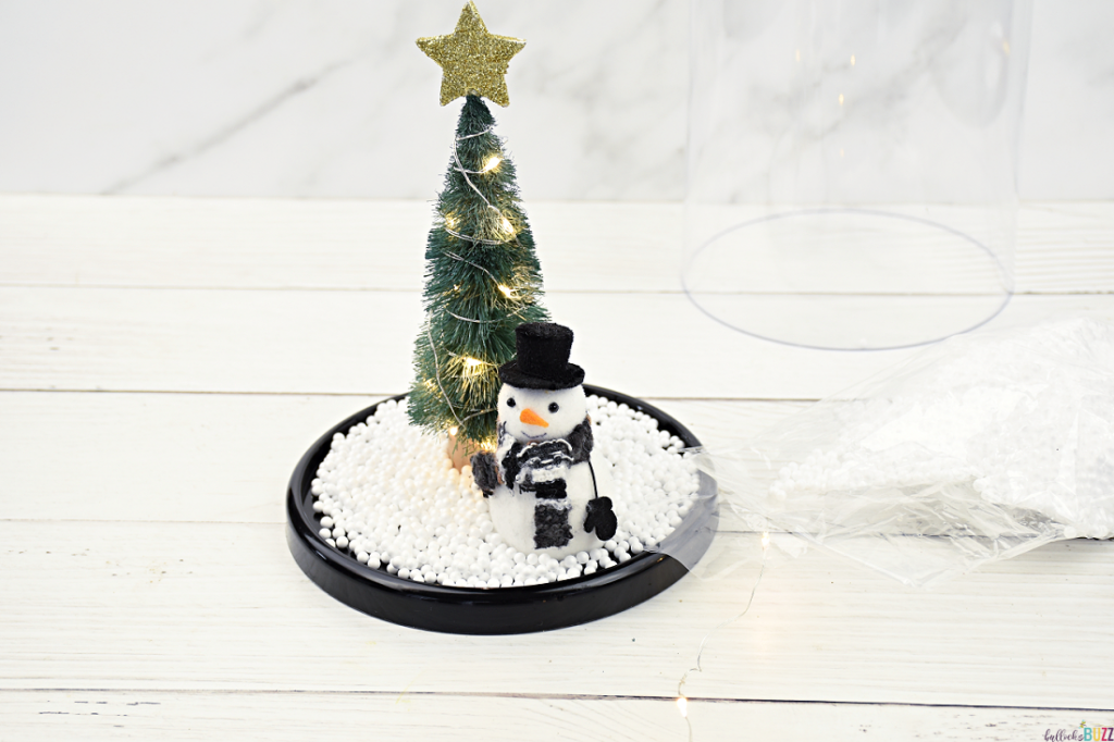 Sprinkling faux snow around the snowman and tree on the Christmas Cloche for a festive and wintry touch 