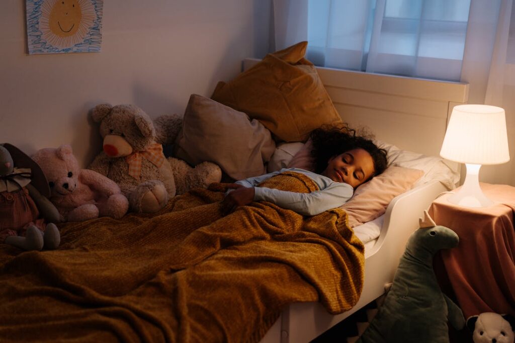 Child asleep in her bed with het beside lamp on