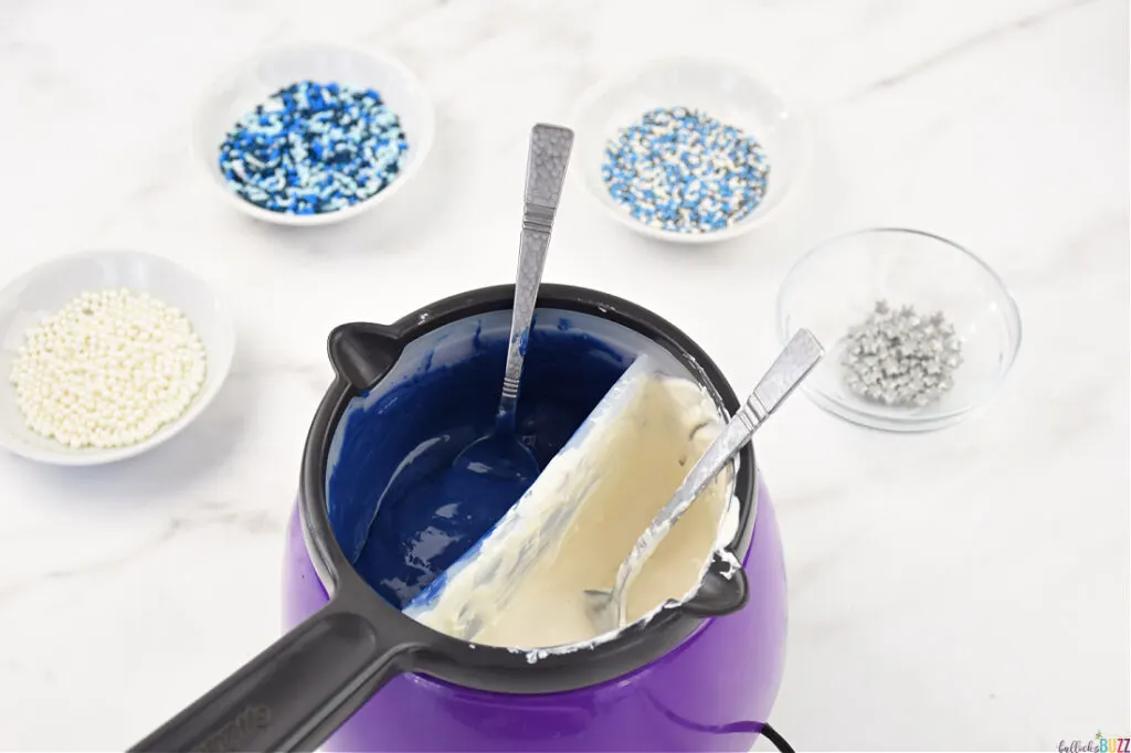 blue and white candy melts in a melting post surrounded with bowls of sprinkles sitting ready to make this homemade Hanukkah candy recipe