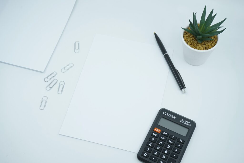 A pencil, calculator and paper on a white tabletop