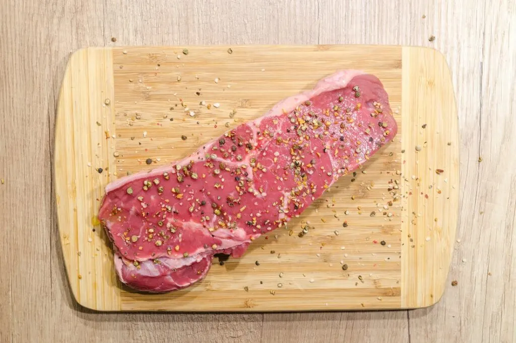piece of seasoned meat on a cutting board that will be made into jerky