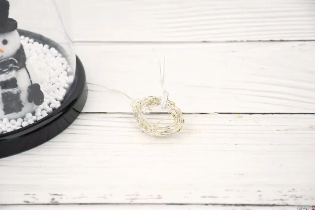 Rolling up excess lights into a loop and securing with a twist tie for a tidy finish in crafting the DIY Christmas Cloche.