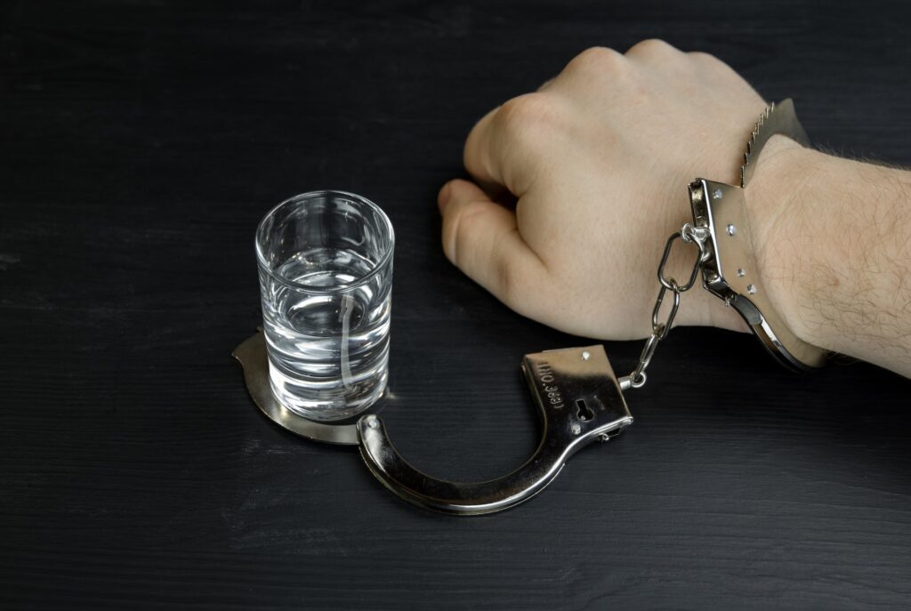 A man's write handcuffed to a shot glass showing how hard being able to stop substance abuse truly is despite these sobriety tips