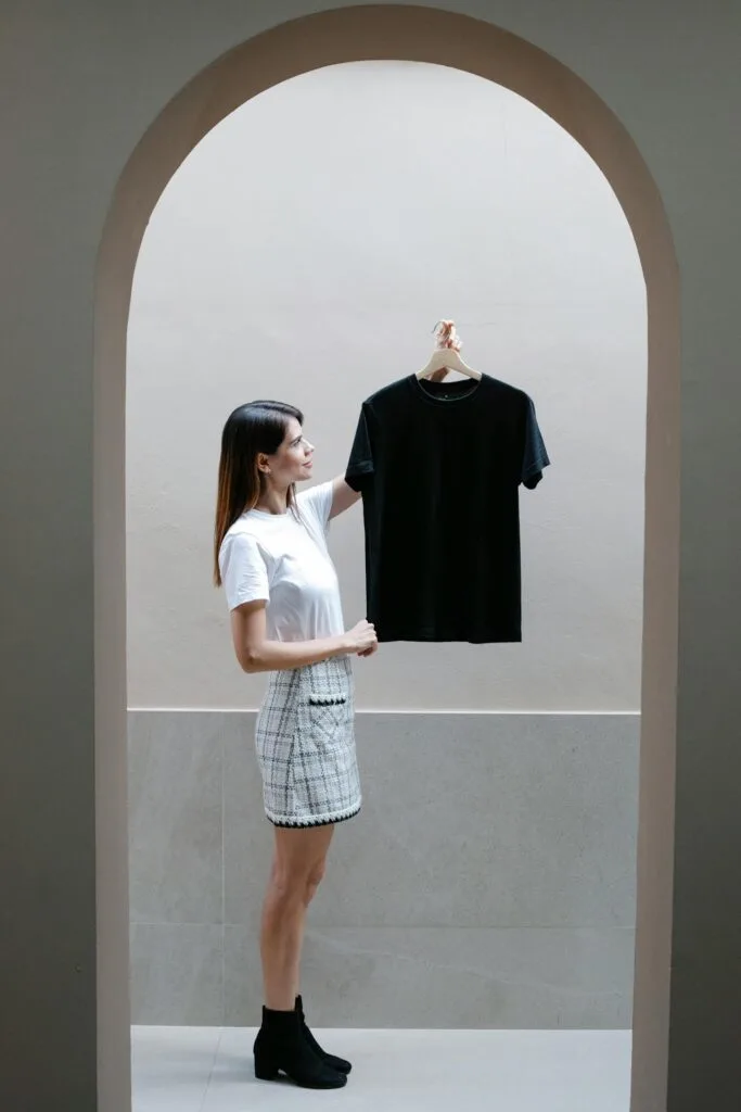 A woman standing in an arched doorway holding up a black t-shirt