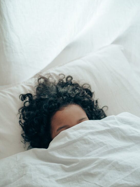 Woman sleeping beneath a white cover. A cozy bedroom is one of several tips to help you sleep better.