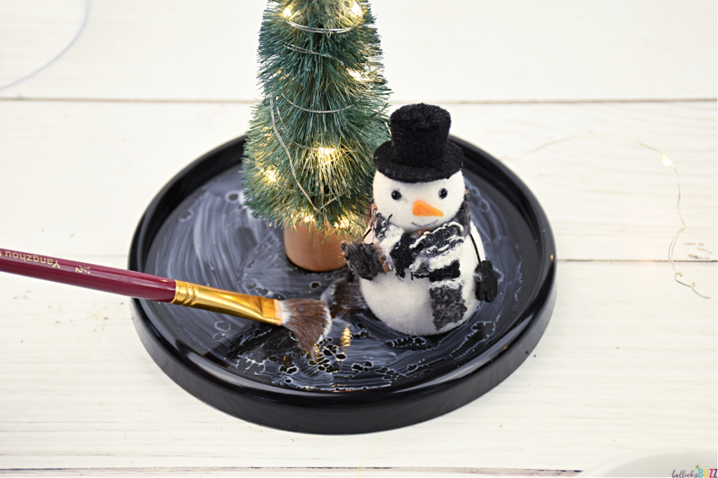 Applying glue around the base of a Christmas tree and snowman using a paintbrush 