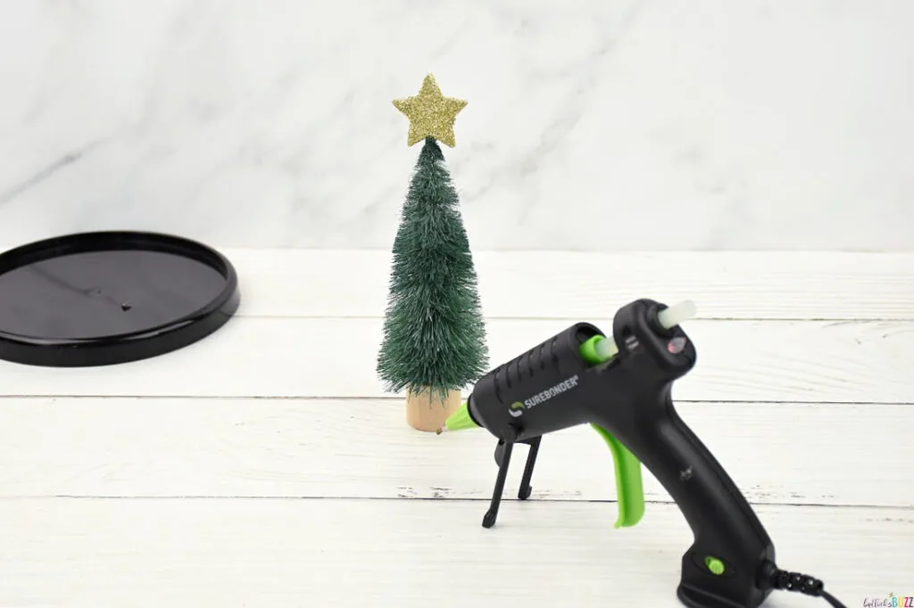 Attaching a mini star to the top of a Christmas tree using a glue gun for DIY Christmas Cloche craft.