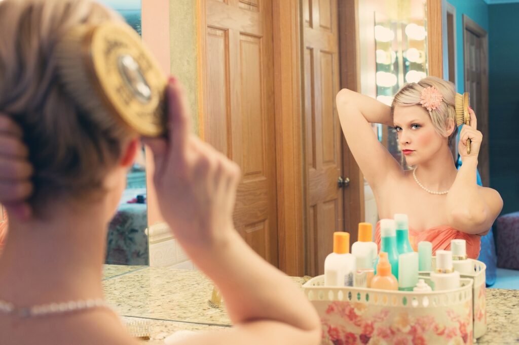 A woman watching herself in the mirror as she brushes her hair. Experimenting with hair and makeup is an empowering part of the personal transformation process.