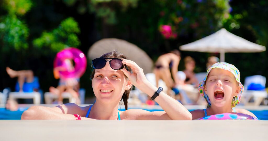 A mother and daughter in the pool hanging on the edge and smiling