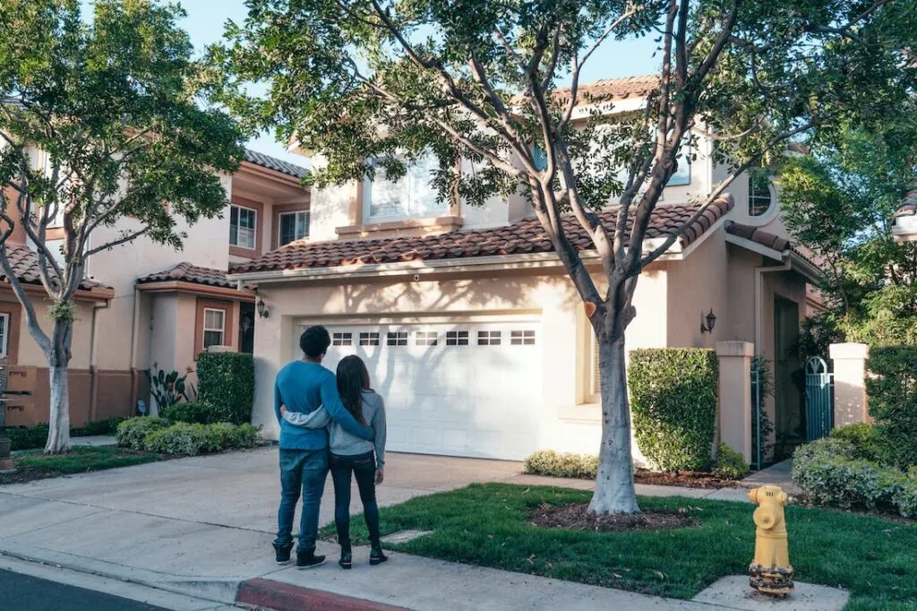 A couple standing arm in arm outside a home after deciding that now is a good time to buy a house