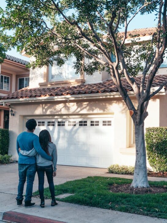 A couple standing arm in arm outside a home after deciding that now is a good time to buy a house