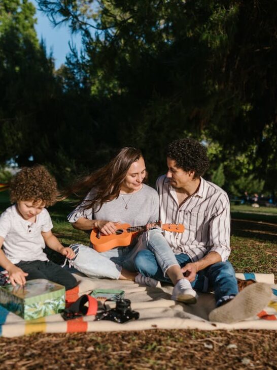 A dad, mom and kid having a picnic on a blanket in a park during their family friendly super bowl getaway weekend.