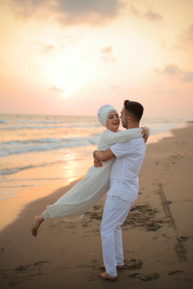 Man holding a woman in his arms and twirling her around while standing on a  beach