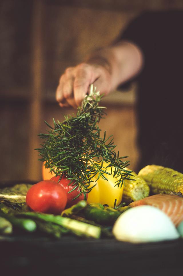 A person adding stems of rosemary to ingredients on a cutting board