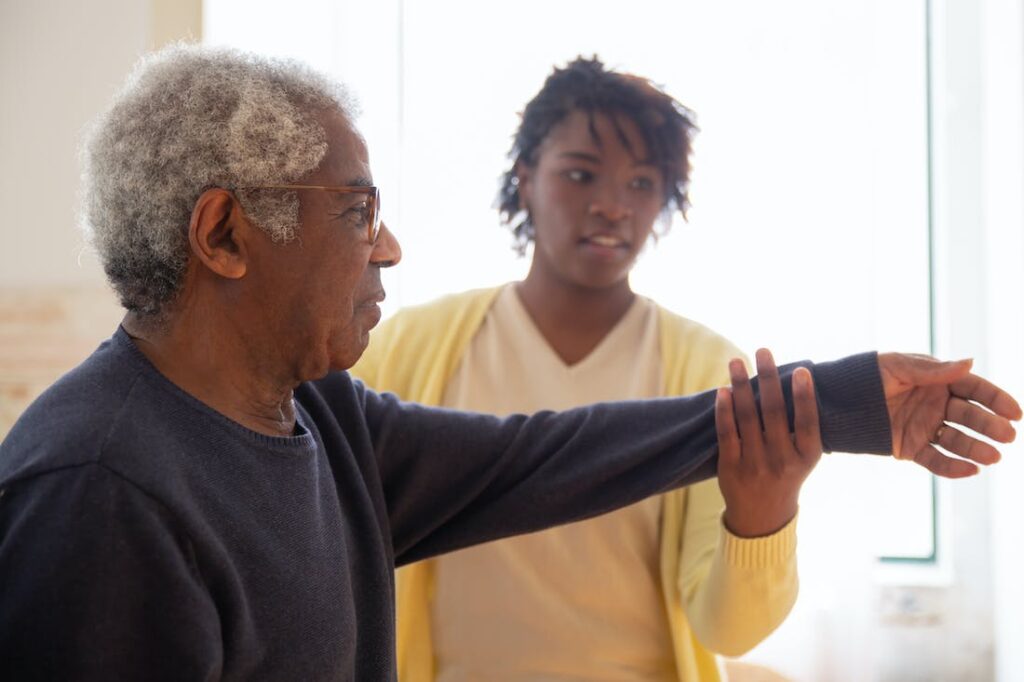 A nurse in a yellow sweater working with an elderly man on his arm range of motion