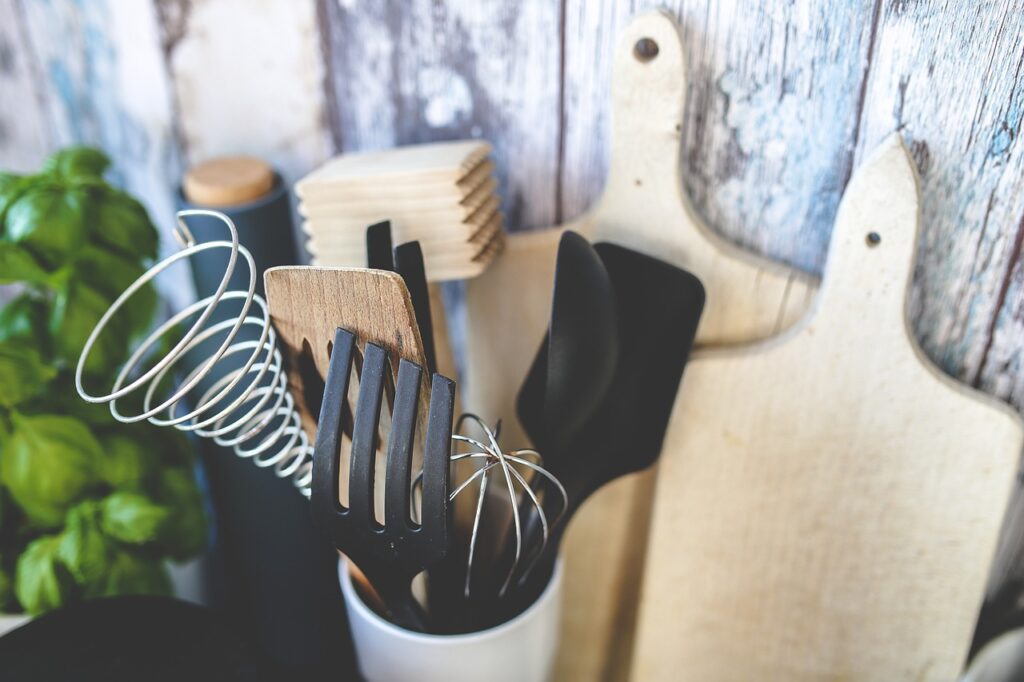 kitchen utensils in a white holder in front of cutting boards and fresh herbs