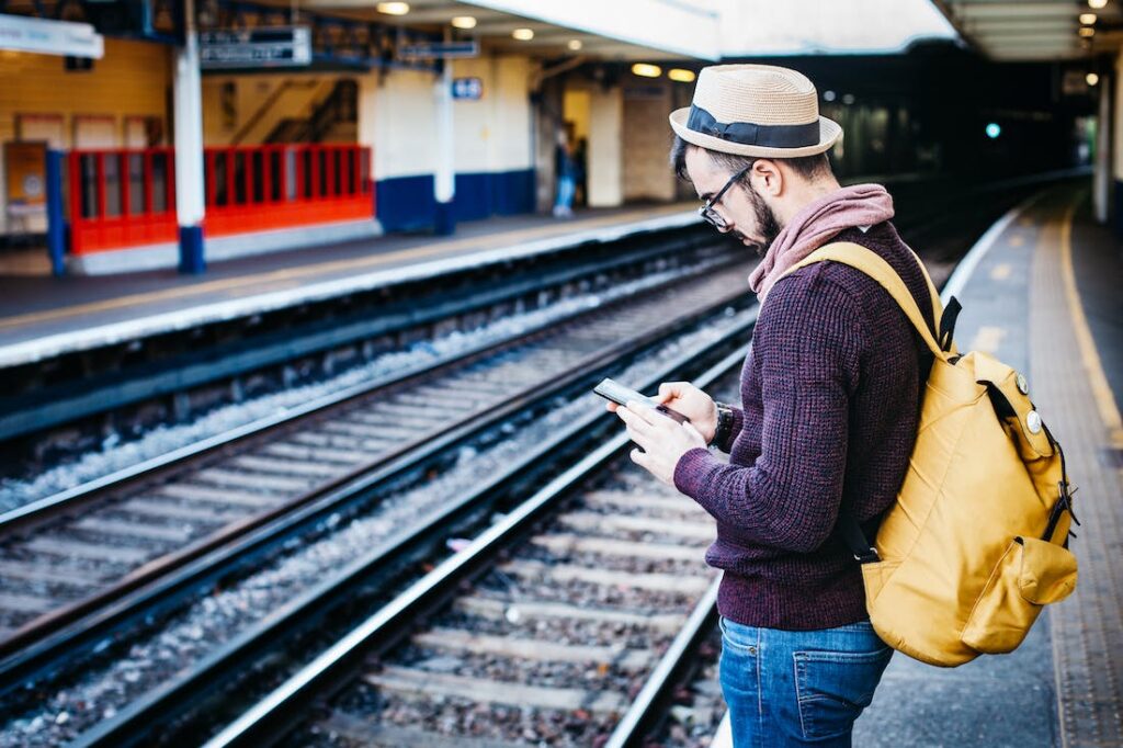 A man on his phone while waiting by the tracks for his train.