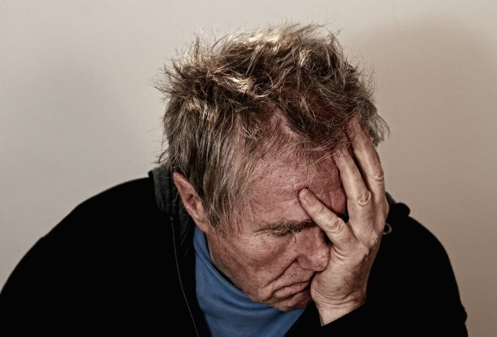 Older man holding his head in his hand suffering from concealed depression