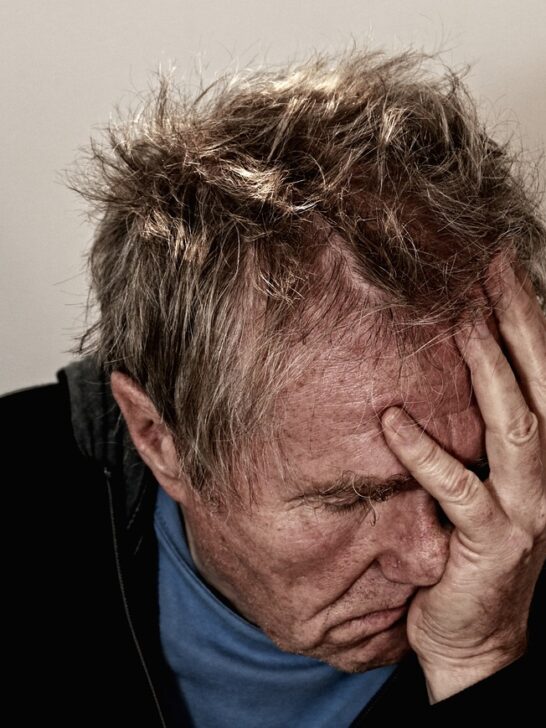Older man holding his head in his hand suffering from concealed depression