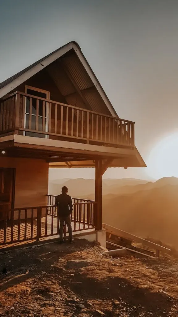 A man standing on the porch of a mountain cabin looking at the mountains. Buying a vacation cabin is one of the most popular real estate investment strategies.