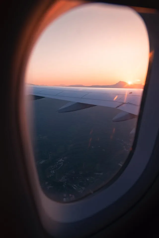 A picture taken from inside an airplane of the wing and sunset while flying over mountains