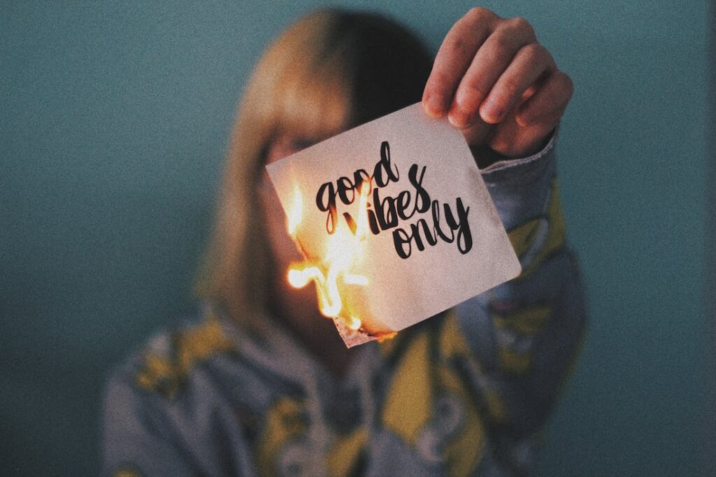 A woman holding a burning piece of note paper with good vibes only written on it