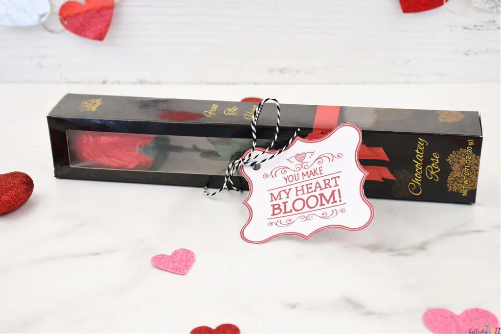 A chocolate rose nestled in a black box, accompanied by a 14 Days of Valentines tag with the message 'You Make My Heart Bloom'.