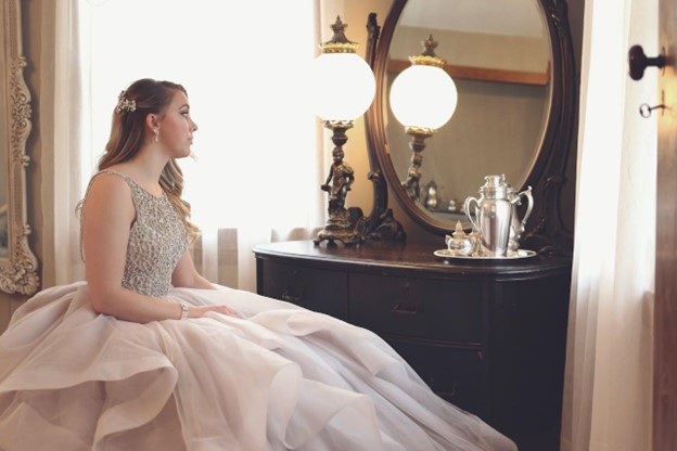 A woman sitting in a formal dress. Here are the differences when it comes to Ball Gowns Vs A-Line Dresses