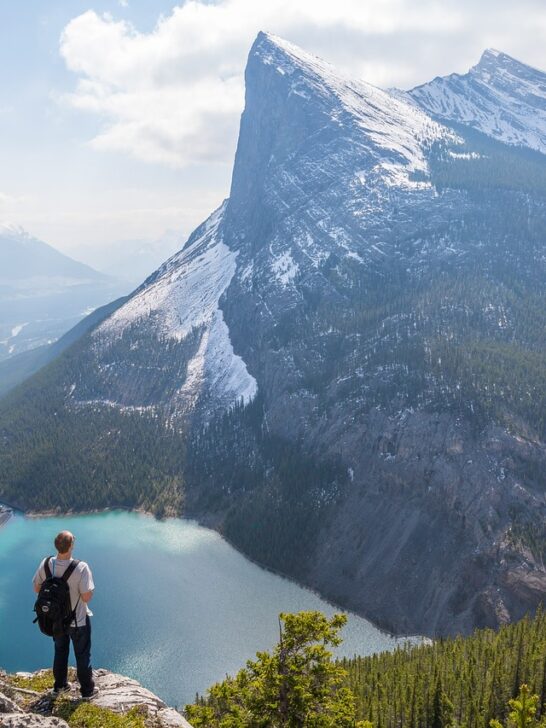 A man standing on a peak overlooking the mountains and a lake in the Canadian Rockies, one of the best places to visit in Canada