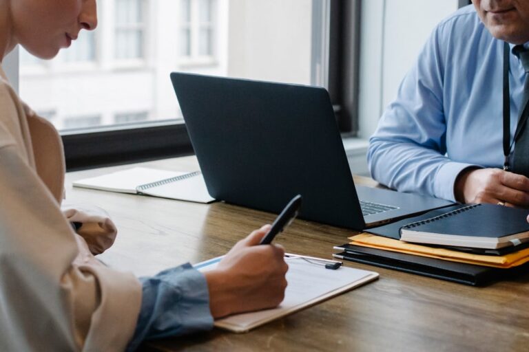 Two people working together on the power of branding with one person writing in a notebook and the other using his laptop.