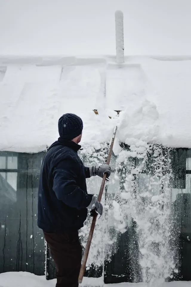 A man removing snow from his roof as part of winter roof maintenance tips.