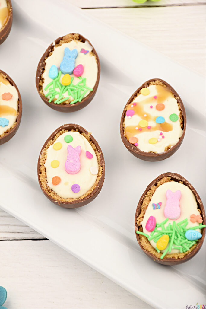 Four cheesecake filled Easter eggs decorated with sprinkles and candy on a white tray